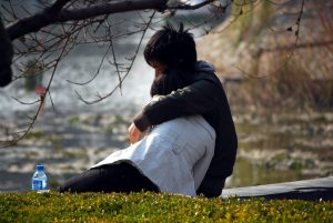 young couple sitting on the ground by water and hugging